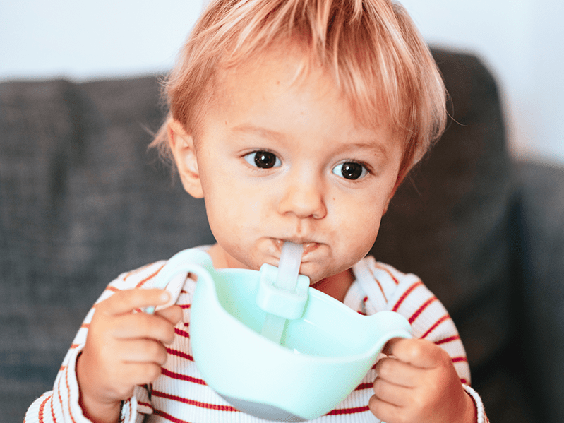 Bébé qui est en train de boire à la paille dans un bol vert menthe